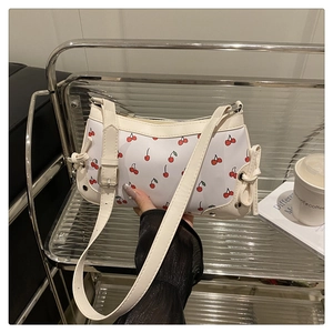Close-up of a white shoulder bag with cherry patterns and side bow drawstring details
