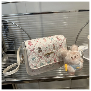Detail of white PU leather bag with cartoon embossed patterns and pink plush bunny charm