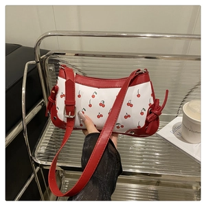 Detail shot of cherry print saddle bag with red leather trim and knot decor on a shelf