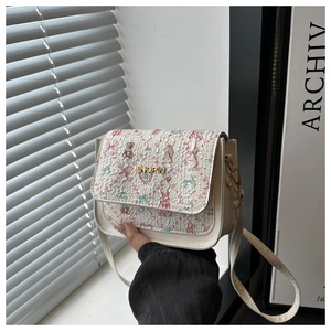 Detail of floral rabbit jacquard pattern and gold metal logo on a cream leather bag