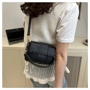 Detail view of black woven crossbody bag with wavy flap edge and gold hardware