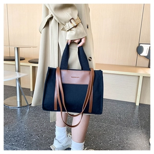 Detail of canvas tote bag with brown leather trim and dual handles shown by model
