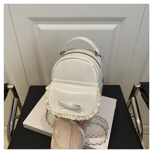 Close-up of white mini backpack featuring lace edges, a bow detail and metal chain strap