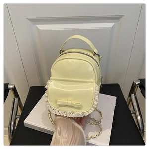 Macro shot of pale yellow backpack featuring lace trim, bow detail, and metal chain strap