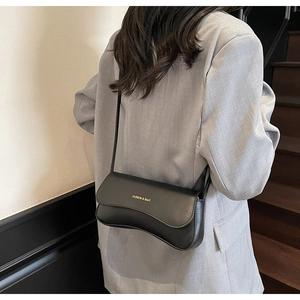 Detail of black crossbody bag with wave flap and gold text on grey blazer model