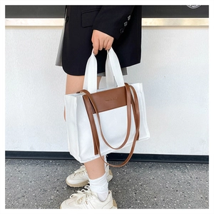 Close-up of canvas tote bag with brown leather handles worn with a black blazer