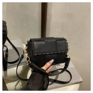 Détail du sac bandoulière en cuir tressé noir avec bordure festonnée et chaîne dorée