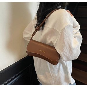 Detail of a brown leather shoulder bag with a knotted strap and gold foil logo text
