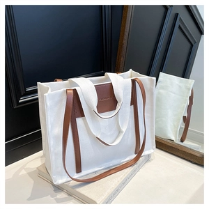 Detail of canvas tote bag with brown leather accents and FASHION BAG logo on a book