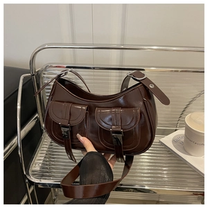 Close-up of brown PU saddle bag with double pockets and silver metal buckles on glass shelf