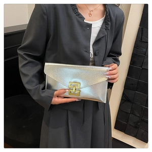 Detail of silver envelope clutch with metallic texture and gold lock held by model