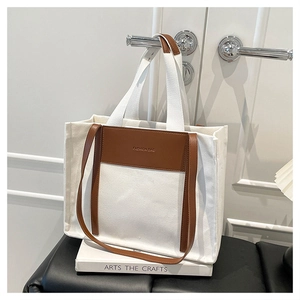 Detail view of canvas tote bag with brown leather panel and adjustable shoulder strap