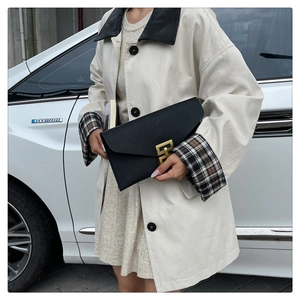 Close-up of black leather envelope clutch with distinctive gold metal geometric clasp detail