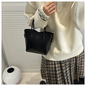 Detail of a black minimalist mini bucket bag with dual handles and side metal D-rings