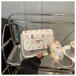 Close-up of white crossbody bag with cute teddy bear prints and plush rabbit charm