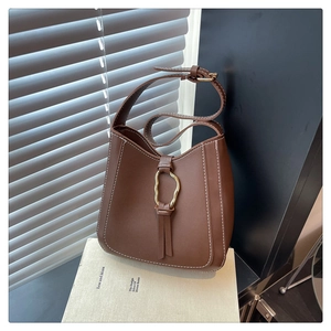 Detalle del bolso tipo cubo de cuero marrón con costuras blancas y hebilla de metal dorada