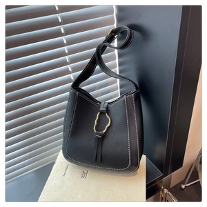Detalle de bolso saco de cuero negro mate con costuras blancas y un anillo de metal dorado