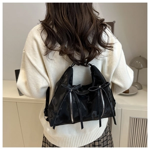 Détail d'un sac cabas noir à nœud avec finition brillante porté sur l'épaule