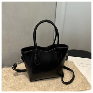 Detail of a black leather bucket bag with FASHION embossing and adjustable strap