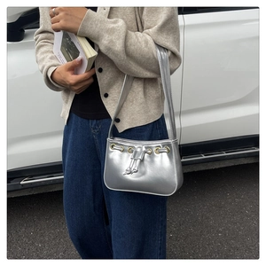 Detail of silver metallic shoulder bag featuring drawstring design and gold ring accent
