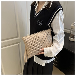 Détail d'une pochette enveloppe matelassée beige avec clous métalliques et dragonne assortie