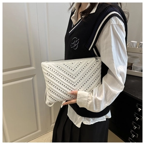 Détail d'une pochette blanche à matelassage en V avec rivets foncés et dragonne latérale