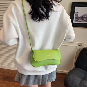 Neon green crossbody bag with gold text lettering worn by model over white clothing