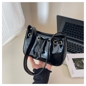 Detail showing high-gloss black patent leather texture and gold hardware on handbag