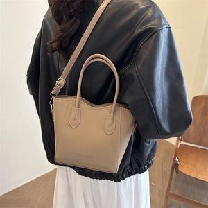 Sac seau en cuir beige avec poignée et texte mode porté sur une veste en cuir noir