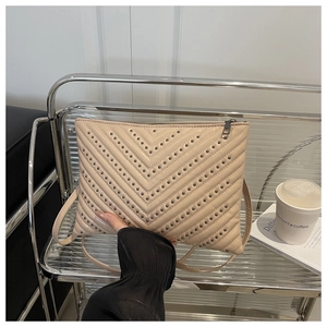 Détail du sac enveloppe matelassé beige avec clous métalliques en V et fermeture éclair