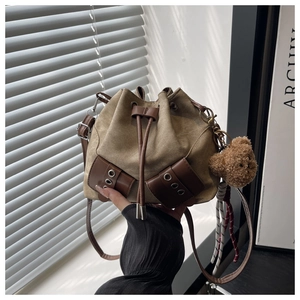 Detail of canvas drawstring bucket bag with leather trim and plush bear charm