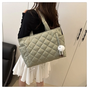 Close-up of light green quilted tote bag with stitching detail and plush toy charm