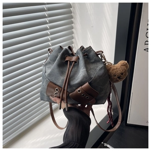 Detail of washed denim bucket bag with brown leather trim and plush bear charm