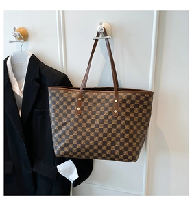 Detail of checkered tote bag with brown leather handles and golden rivet reinforcements