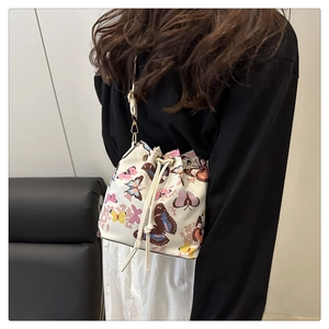 Detail of crossbody bucket bag with butterfly print and drawstring closure on model