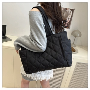 Detail view of a large black quilted tote bag with diamond stitching and side pockets