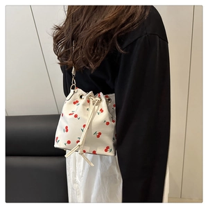 Side view of white drawstring bucket bag with red cherry print and slender shoulder strap