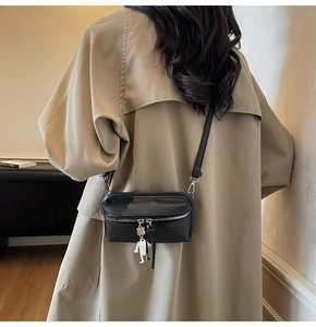 Detail of black square crossbody bag with a unique robot charm on khaki trench coat