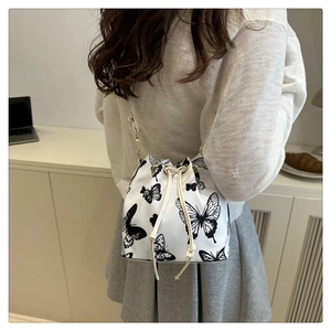 Detail of white drawstring bucket bag with black butterfly print and gold chain strap