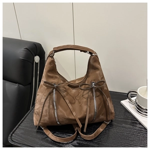 Detailansicht der dunkelbraunen Wildledertasche mit Metallreißverschlüssen und Zierschleifen