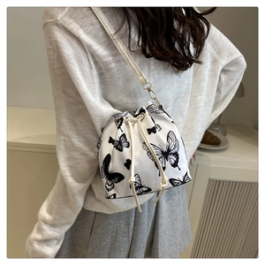 Detail of white drawstring bucket bag with black butterfly print on model shoulder