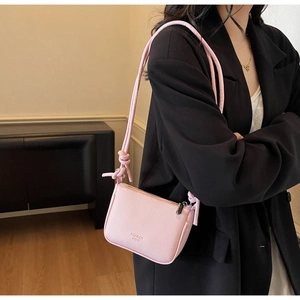 Detail of light pink pebble leather bag featuring stylish knotted strap and metal zipper
