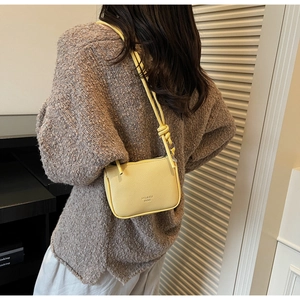 Detail of yellow pebbled leather crossbody bag with decorative knot on shoulder strap