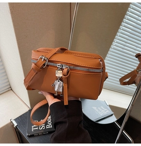 Detail of a brown leather crossbody bag featuring a silver robot pendant and adjustable strap