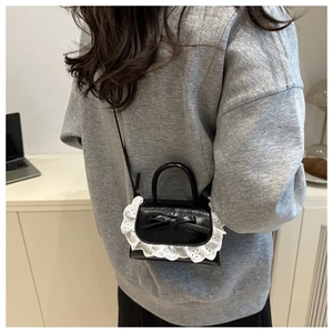 Detailed back view of a mini black crossbody bag with lace trim and bow on a model