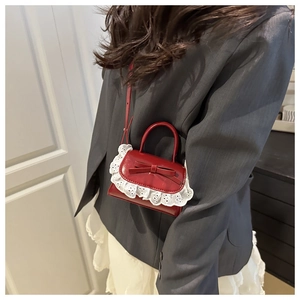 Detail of red bow mini shoulder bag with white lace trim and smooth finish