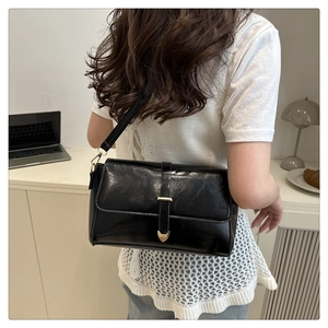 Detail of black faux leather crossbody bag featuring a golden heart lock and decorative strap