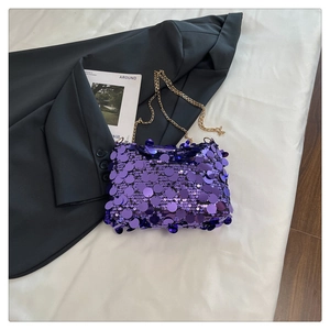 Detail of purple sequin handbag with gold chain strap on white fabric background