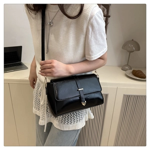 Close-up of black crossbody bag with golden heart buckle and glossy leather texture