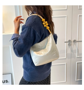 Detail of white embossed shoulder bag featuring unique yellow wooden bead strap accents